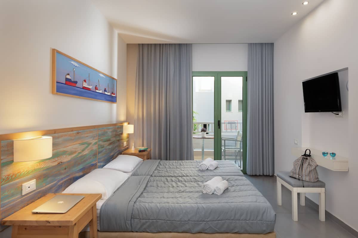 Ett hotellrum med en säng, ett skrivbord, en tv och en balkong med gardiner.