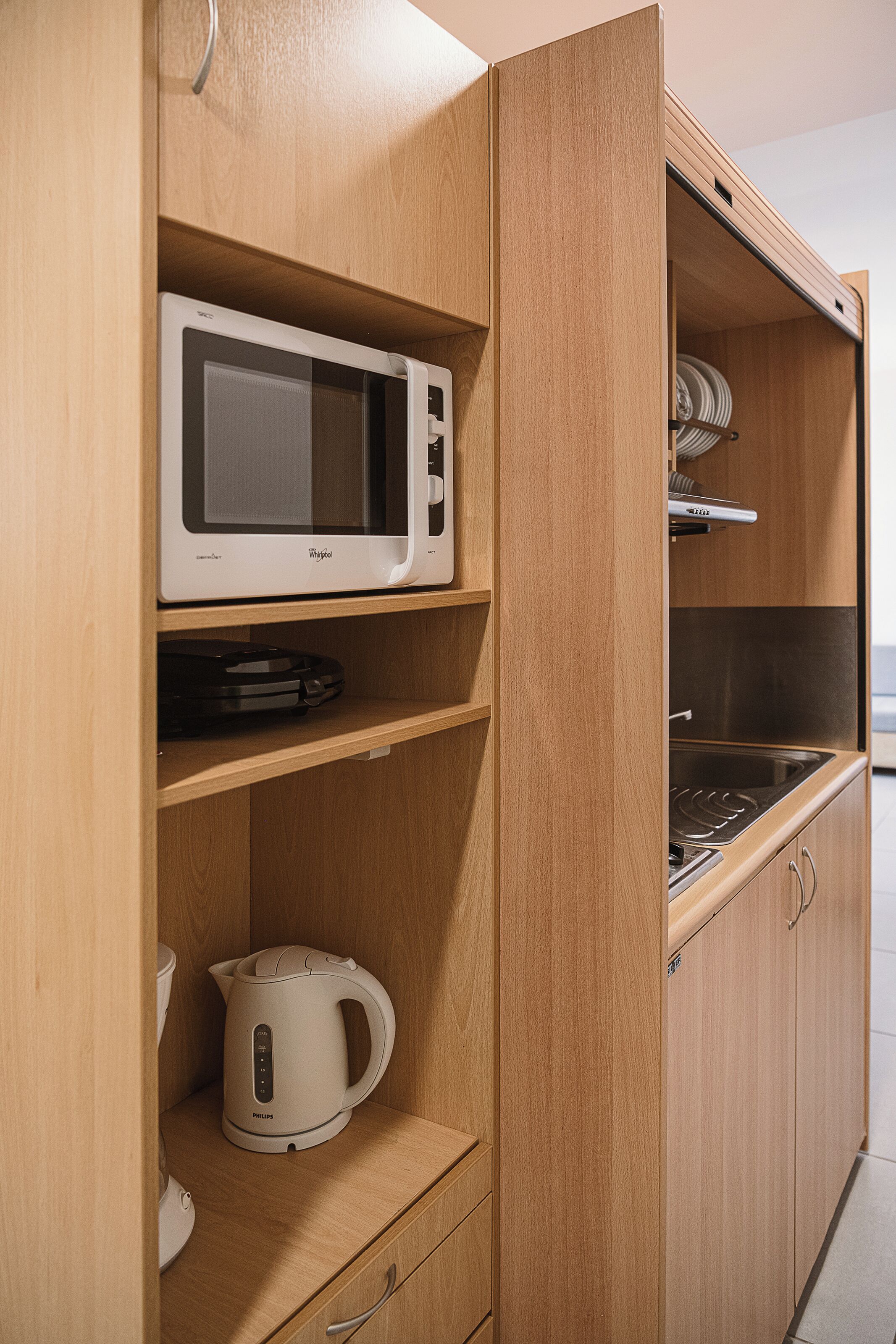 A kitchen with wooden cabinets, a microwave, a kettle, and a stove.