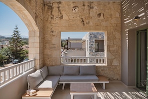 A balcony with a stone wall, a cushioned seating area, and a view of a building with a balcony. - Erato Beach Hotel Adults Only (Platanias)