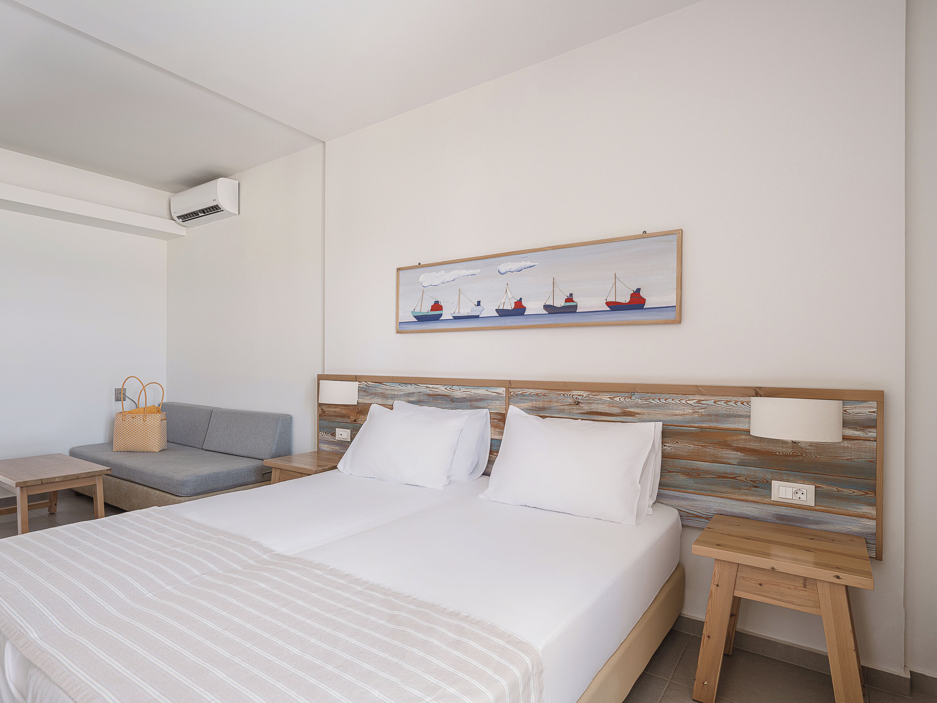 A hotel room with a bed, a nightstand, a lamp, a painting, and a wall-mounted air conditioner.