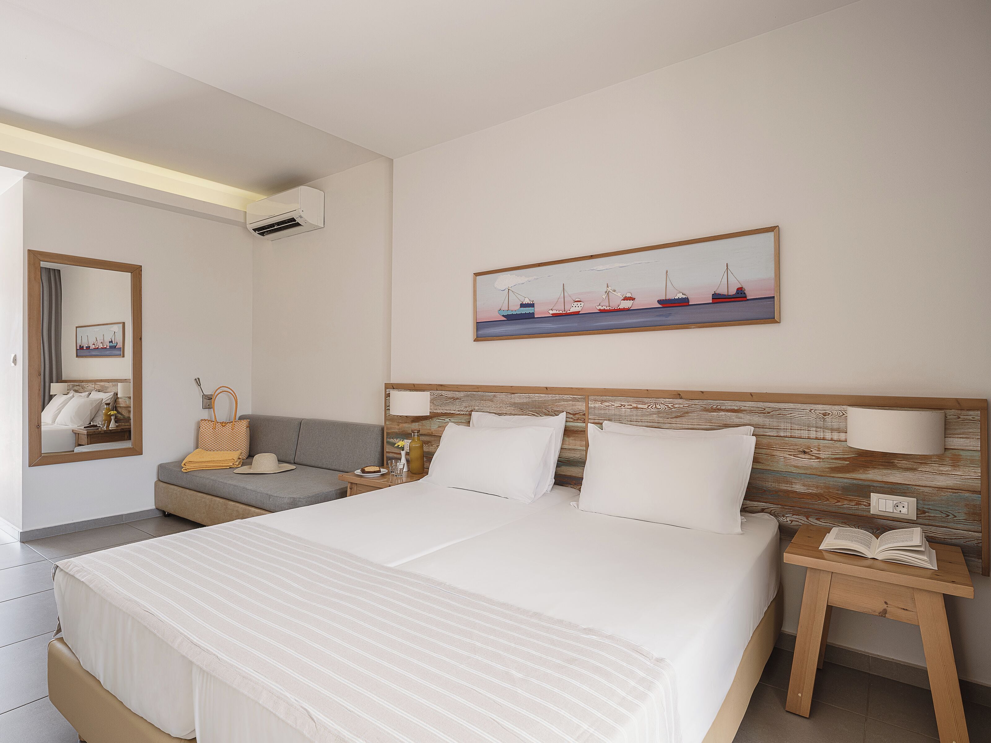 Una habitación de hotel con una cama grande, una mesita de noche con una lámpara, un sofá, una pequeña mesa con un sombrero y una botella, y un cuadro en la pared.