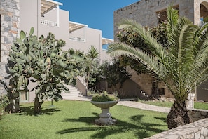 A courtyard with a cactus, palm tree, and a planter with flowers. - Erato Beach Hotel Adults Only (Platanias)