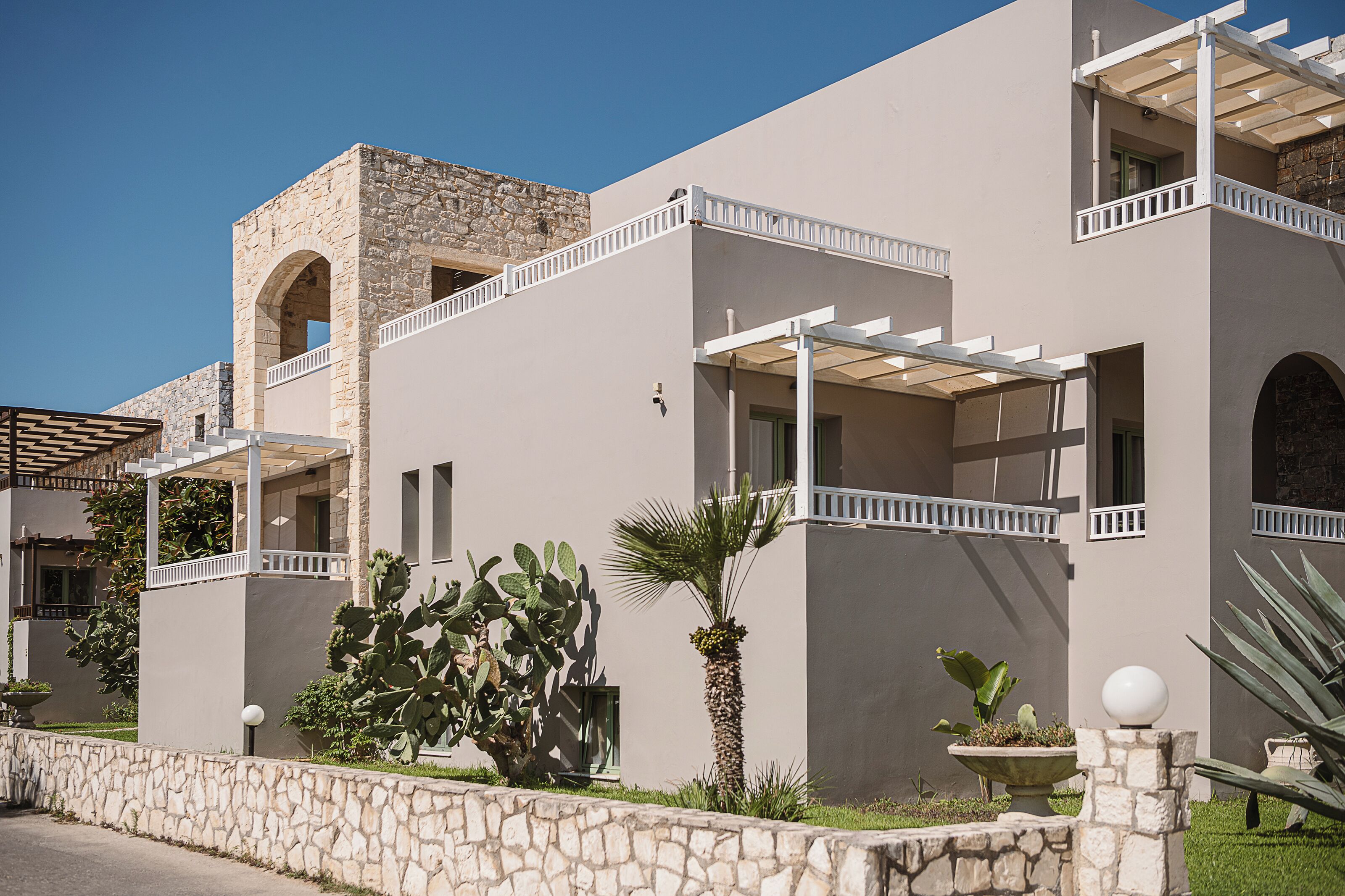 A modern building with a stone facade, multiple balconies, and a courtyard with cacti and palm plants.