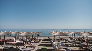 A beach with rows of sun loungers and thatched umbrellas. - Erato Beach Hotel Adults Only (Platanias)