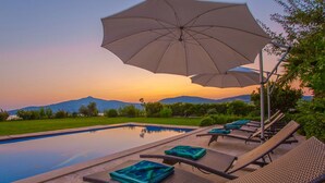 Un espace aménagé au bord de la piscine, avec des chaises longues et des parasols, une vue dégagée sur les montagnes et une pelouse bien entretenue.