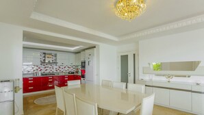 Une cuisine moderne avec des meubles blancs, un plan de travail rouge et un coin repas comprenant une table et des chaises blanches.