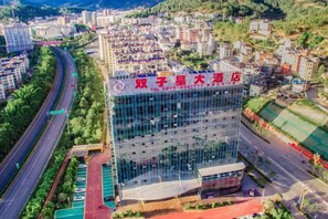 A modern hotel building with a glass facade, located in a city with a surrounding road and greenery. - Shuangzixing Hotel (Mojiang)