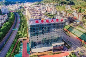 A modern hotel building with a glass facade, located in a city with a surrounding road and greenery.