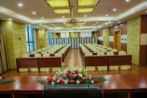A conference room with rows of chairs, a long table with a floral centerpiece, and a ceiling with recessed lighting. - Shuangzixing Hotel (Mojiang)