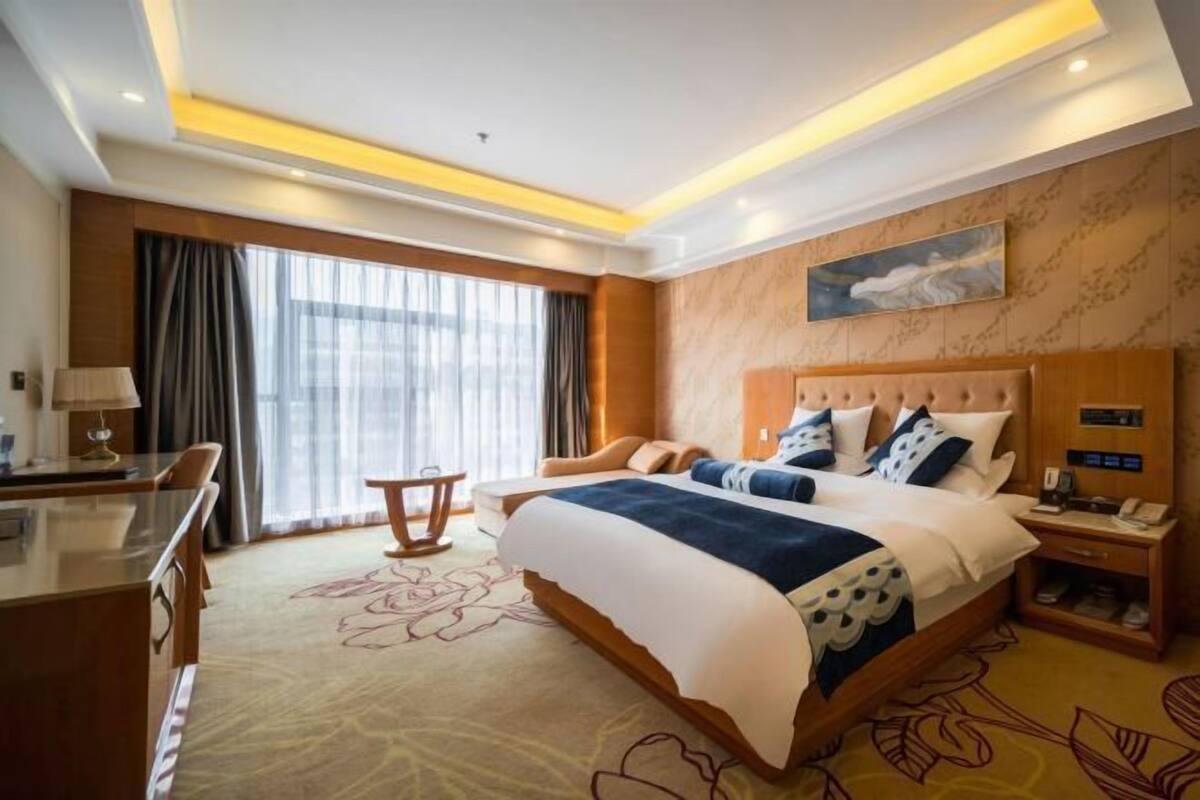 A hotel room with a large bed, a desk, a chair, a nightstand, and a painting on the wall.