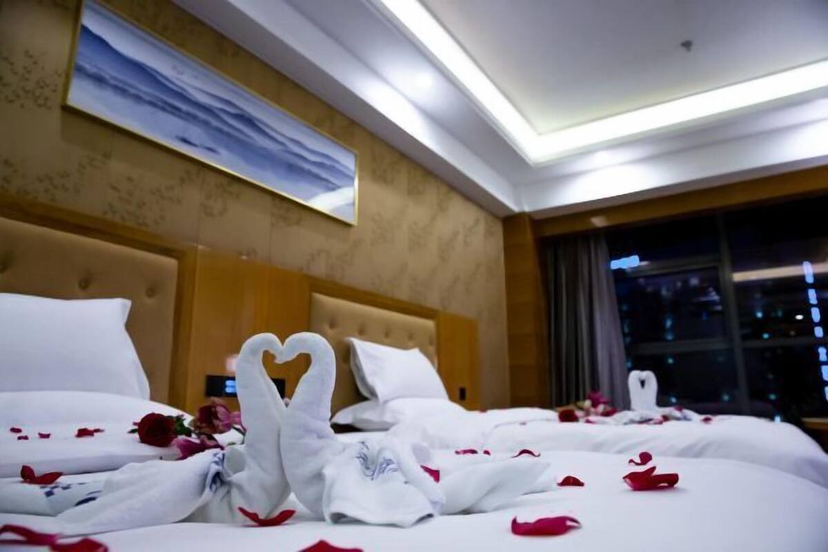 A hotel room with a large bed, a painting on the wall, and a view of the city at night.