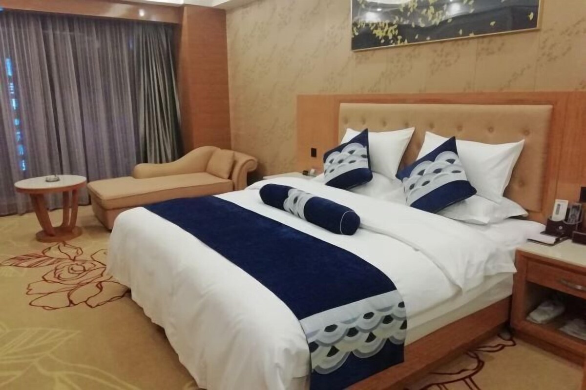 Quarto de hotel com uma cama grande, uma mesinha pequena, um sofá e uma mesinha de cabeceira.