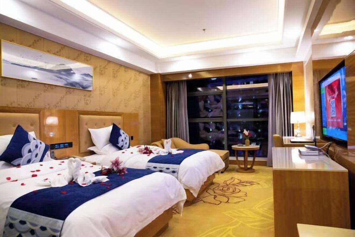 A hotel room with two beds, a television, a desk, and a large window.