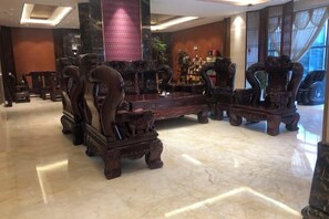 Un hall con muebles de madera ornamentada, suelo de mármol y ventanas amplias.