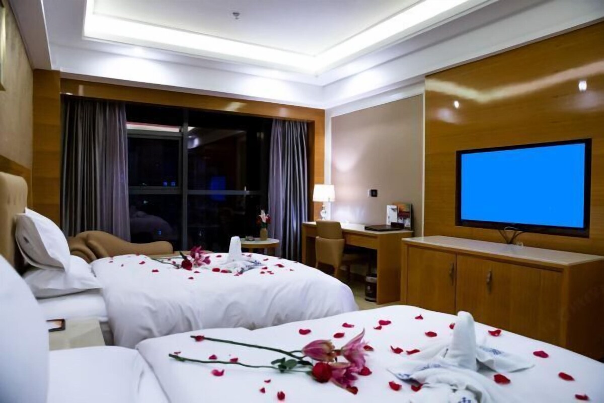 Quarto de hotel com duas camas, uma escrivaninha, uma televisão e uma janela com cortinas.