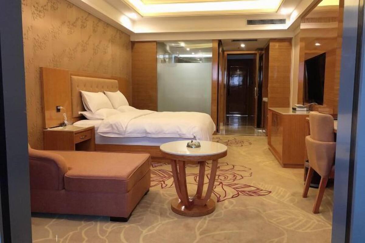 A hotel room with a bed, bedside table, chair, round table, and a desk with a chair.