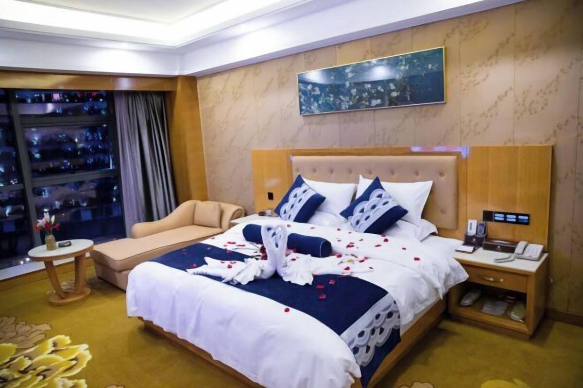 A hotel room with a large bed, a sofa, a small table, a nightstand, and a window with a view of the city.