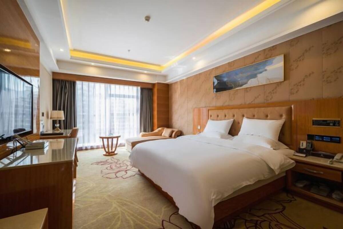 A hotel room with a large bed, a desk, a chair, and a television.