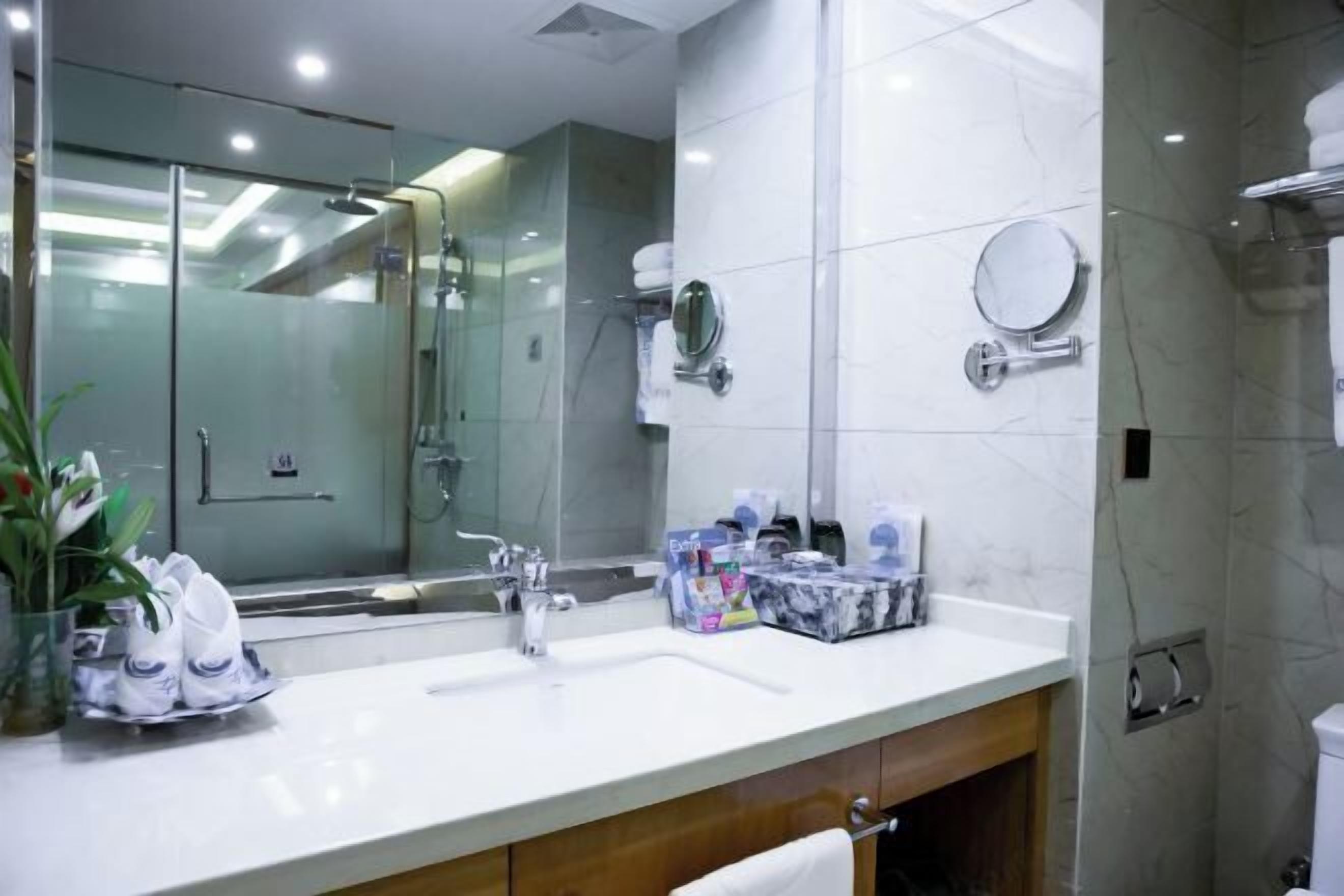 Un baño moderno con cabina de ducha de vidrio, un espejo grande y un lavamanos blanco con artículos de aseo.