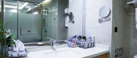 Un baño moderno con cabina de ducha de vidrio, un espejo grande y un lavamanos blanco con artículos de aseo.