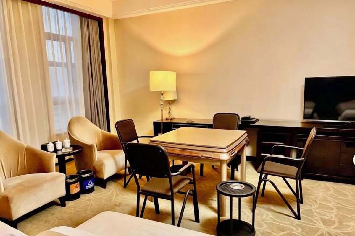A hotel room with a sofa, a dining table with chairs, a TV, and a lamp.