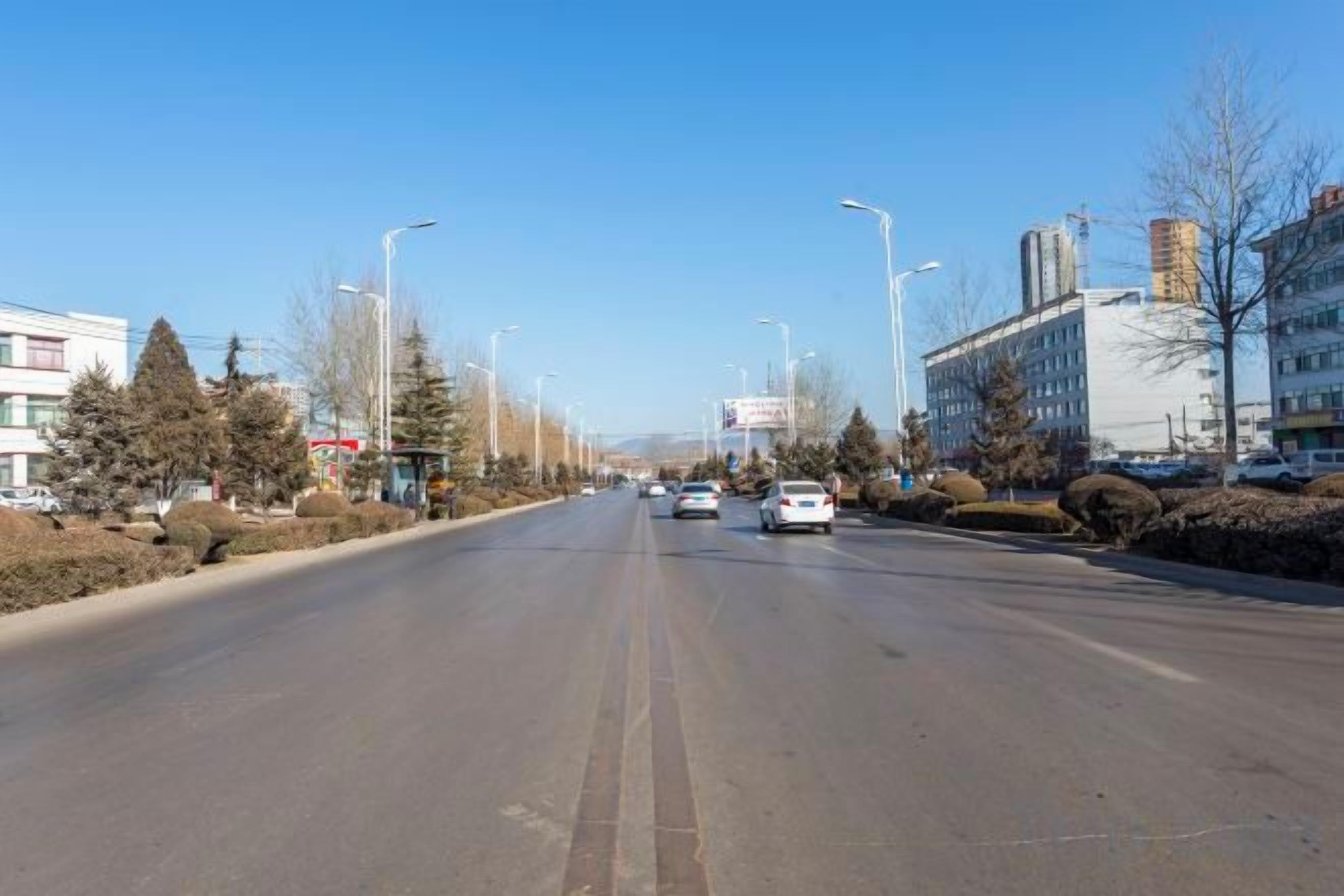 A wide road with vehicles, buildings, and trees on both sides.