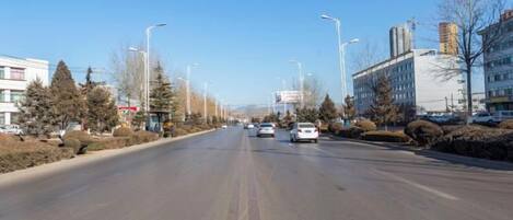 A wide road with vehicles, buildings, and trees on both sides.