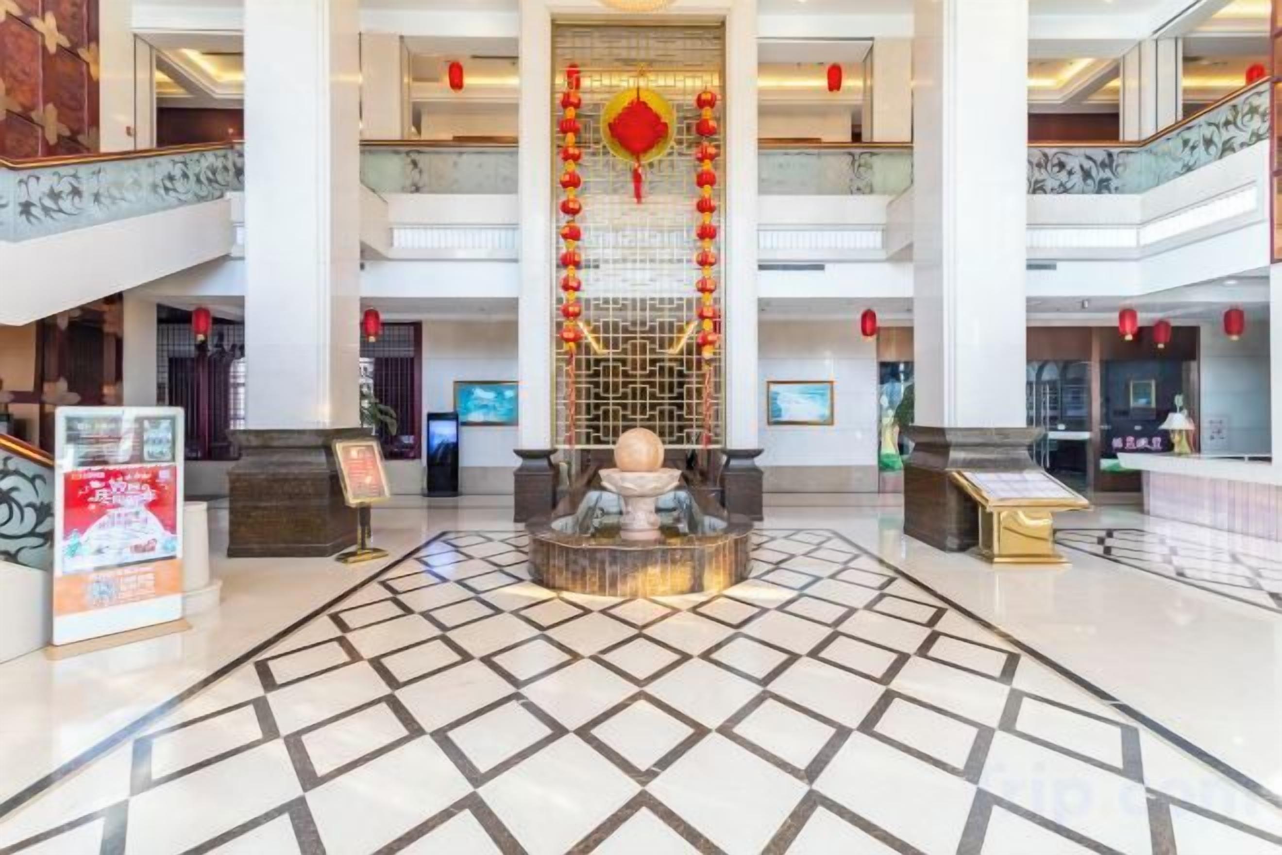 A spacious lobby with a central decorative column, multiple floors, and a tiled floor.