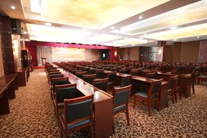 A conference room with rows of tables and chairs, a stage with curtains, and a carpeted floor. - Jinxin Hotel (Xiangyuan)