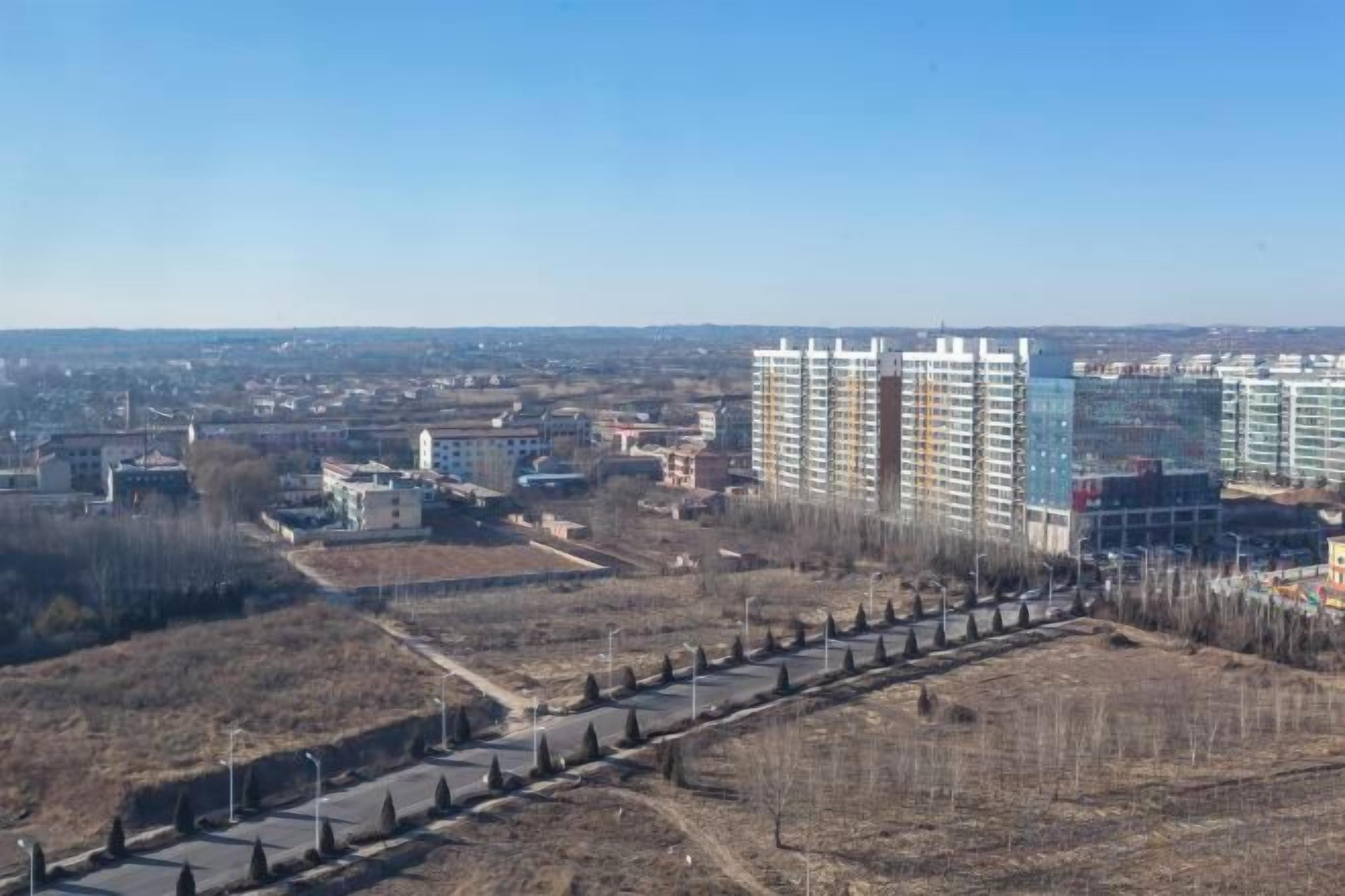 A high-rise building complex with multiple floors, surrounded by open land and a clear sky.