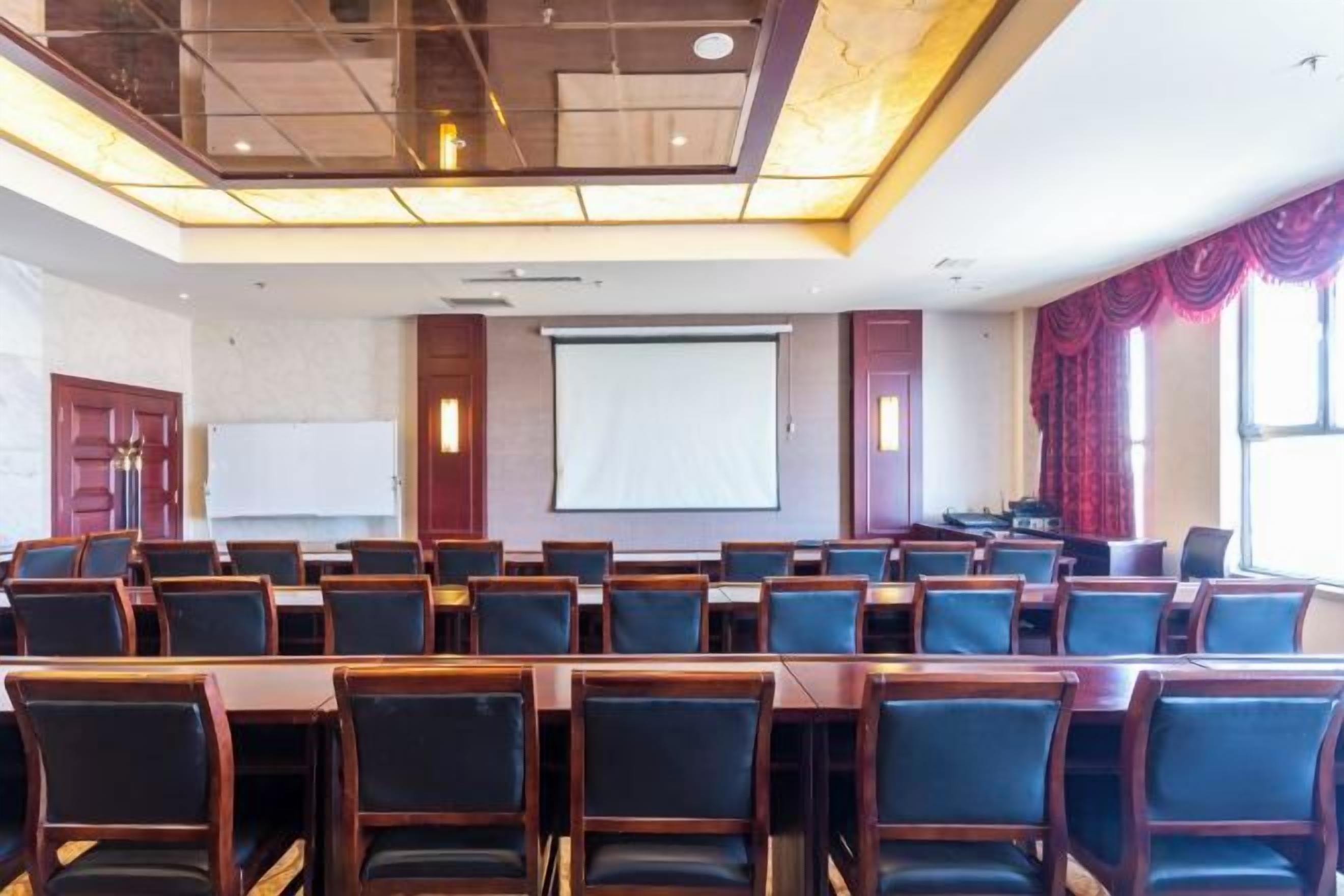 A conference room with rows of chairs, a projector screen, and a large window with curtains.