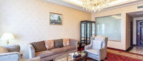 A spacious living area with a large chandelier, a sofa set, a glass coffee table, and a patterned carpet.