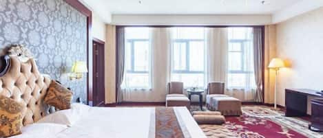Habitación de hotel con una cama grande, un candelabro, un escritorio y vistas a la ciudad a través de amplios ventanales.