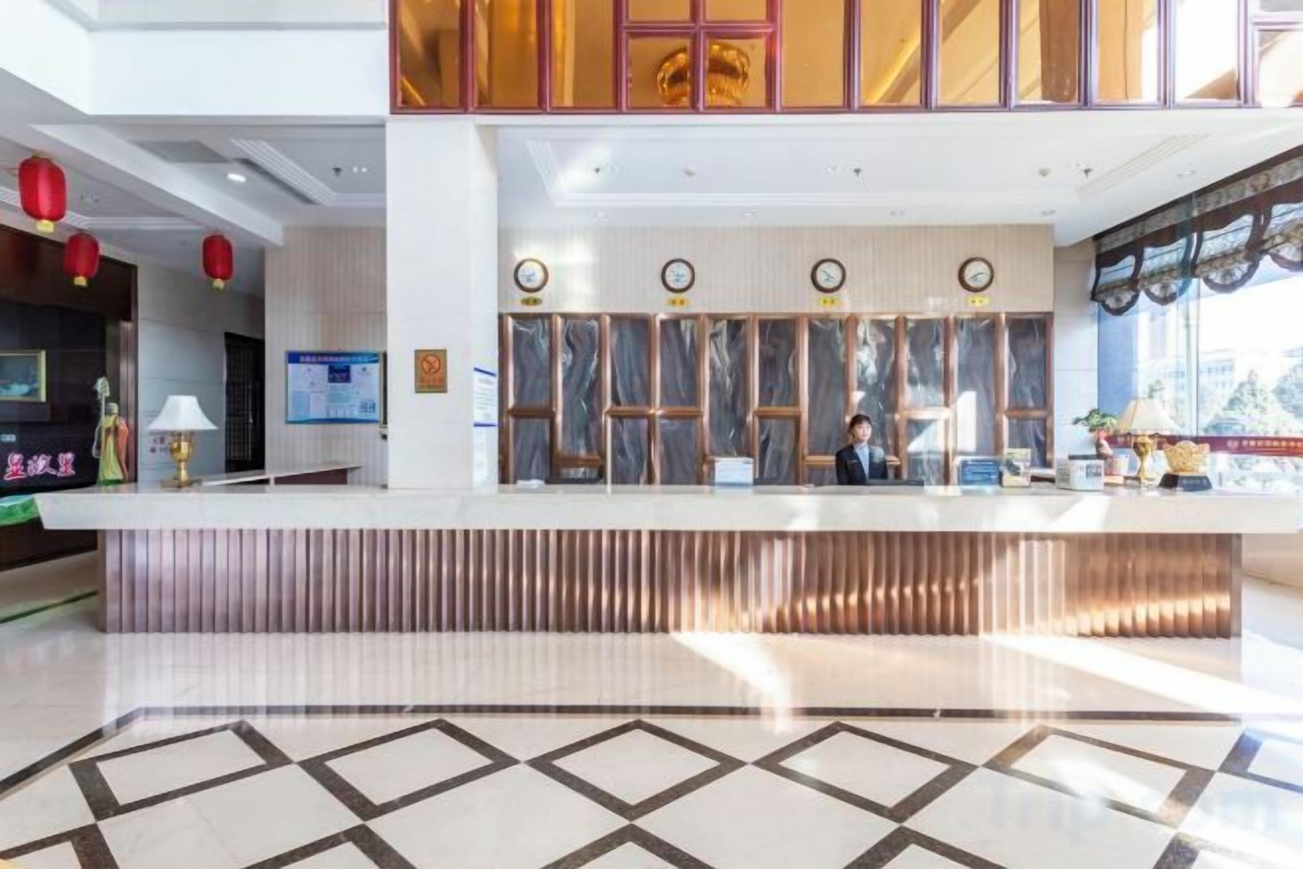 Uma área de recepção de hotel com balcão, recepcionista e uma grande janela.