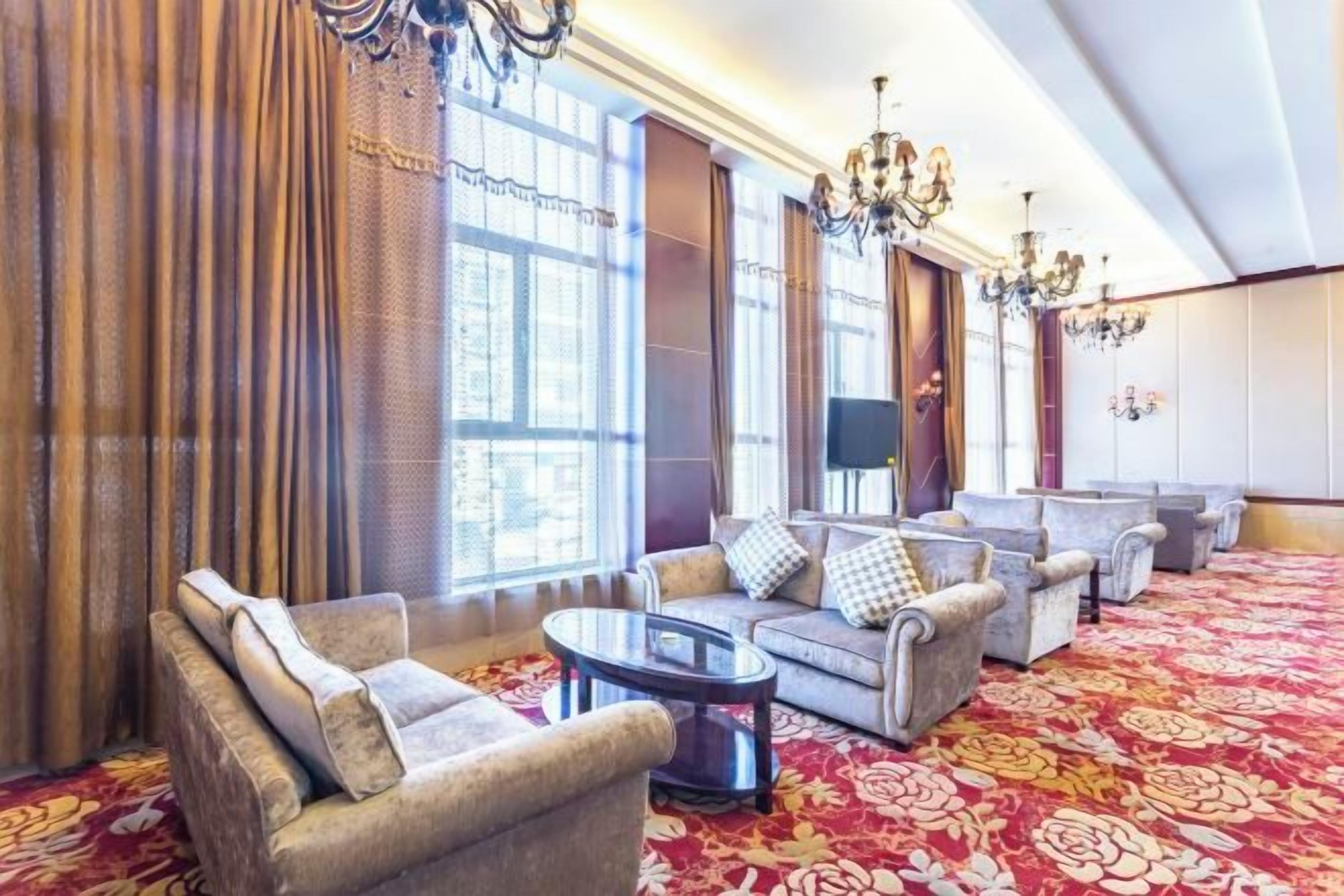 A spacious lobby with a red carpet, multiple seating areas, and large windows with curtains.
