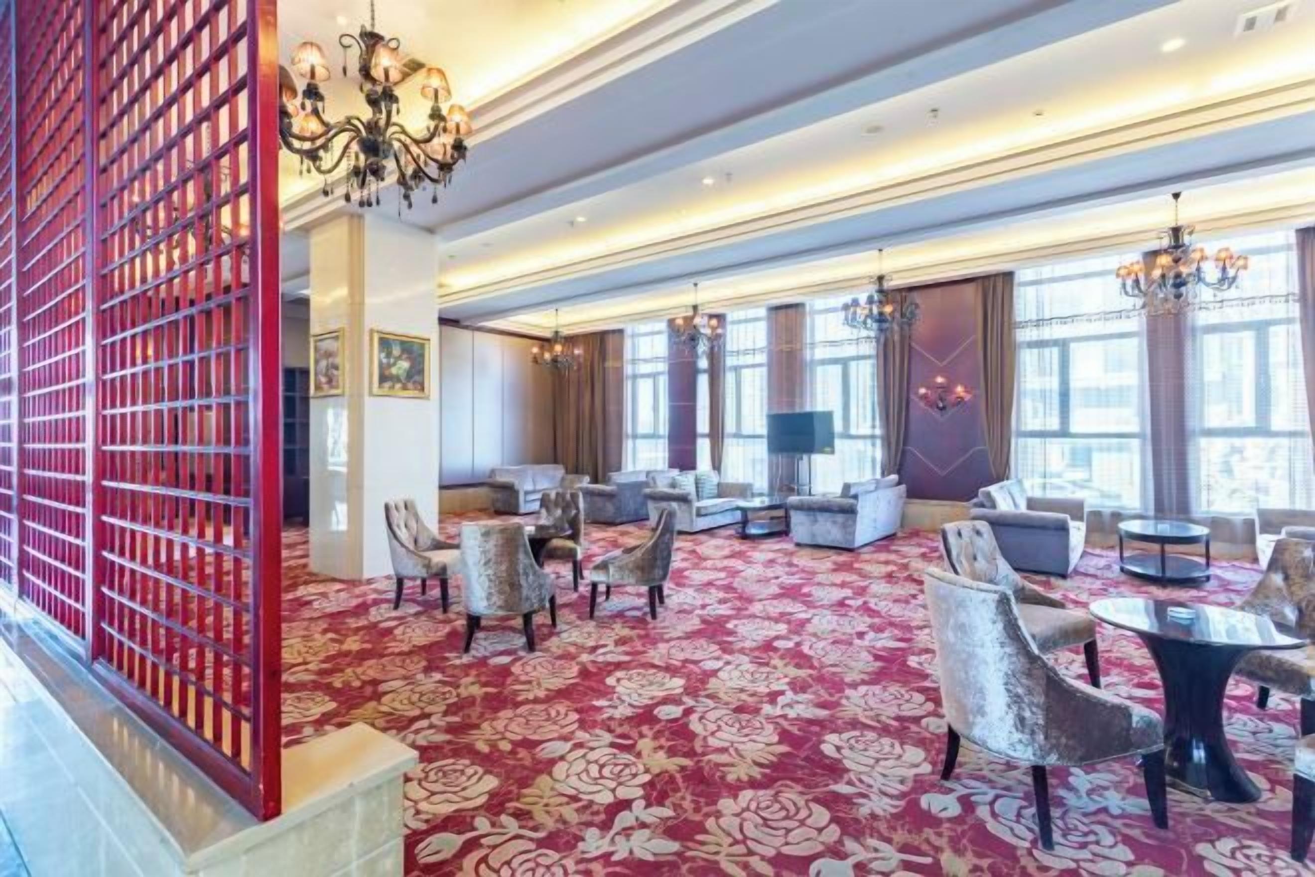 Un hall de hotel con alfombra roja, varias zonas de estar y una gran lámpara de araña.
