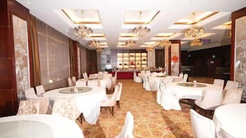 A banquet hall with round tables and chairs, a patterned carpet, and chandeliers.