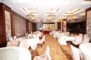 A banquet hall with round tables and chairs, a patterned carpet, and chandeliers. - Jinxin Hotel (Xiangyuan)