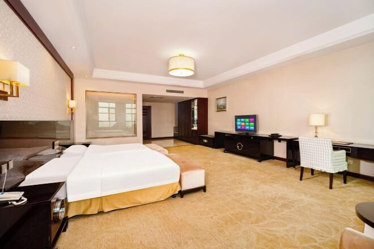 A hotel room with a large bed, a desk, a chair, a television, and a lamp.