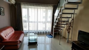A modern living room with a red sofa, a glass coffee table, a flat-screen TV, and a staircase with a railing. - Fubang Hotel Apartment (Suifenhe)