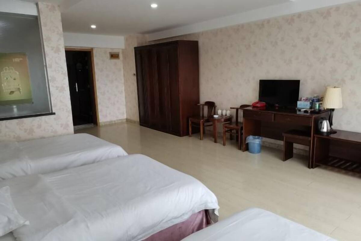 A hotel room with two beds, a desk with a TV, a wardrobe, and a small table with a lamp.