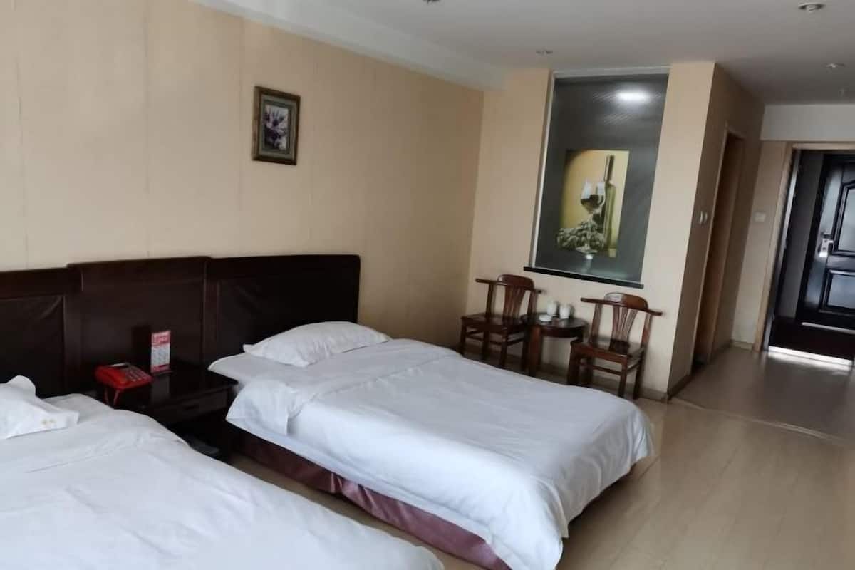 A hotel room with two beds, a small table, two chairs, a framed picture on the wall, and a door leading to another room.