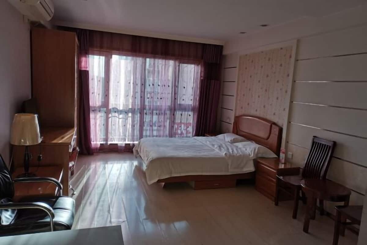 A hotel room with a bed, a desk, a chair, a lamp, and a window with curtains.