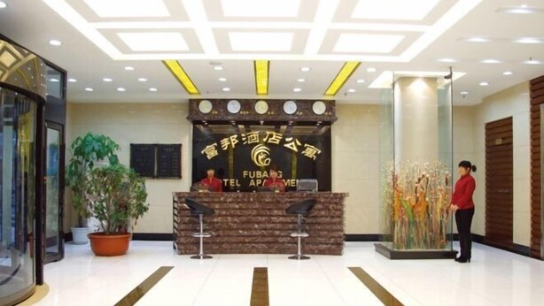 A hotel reception area with a reception desk, two bar stools, a potted plant, and a receptionist. - Fubang Hotel Apartment (Suifenhe)