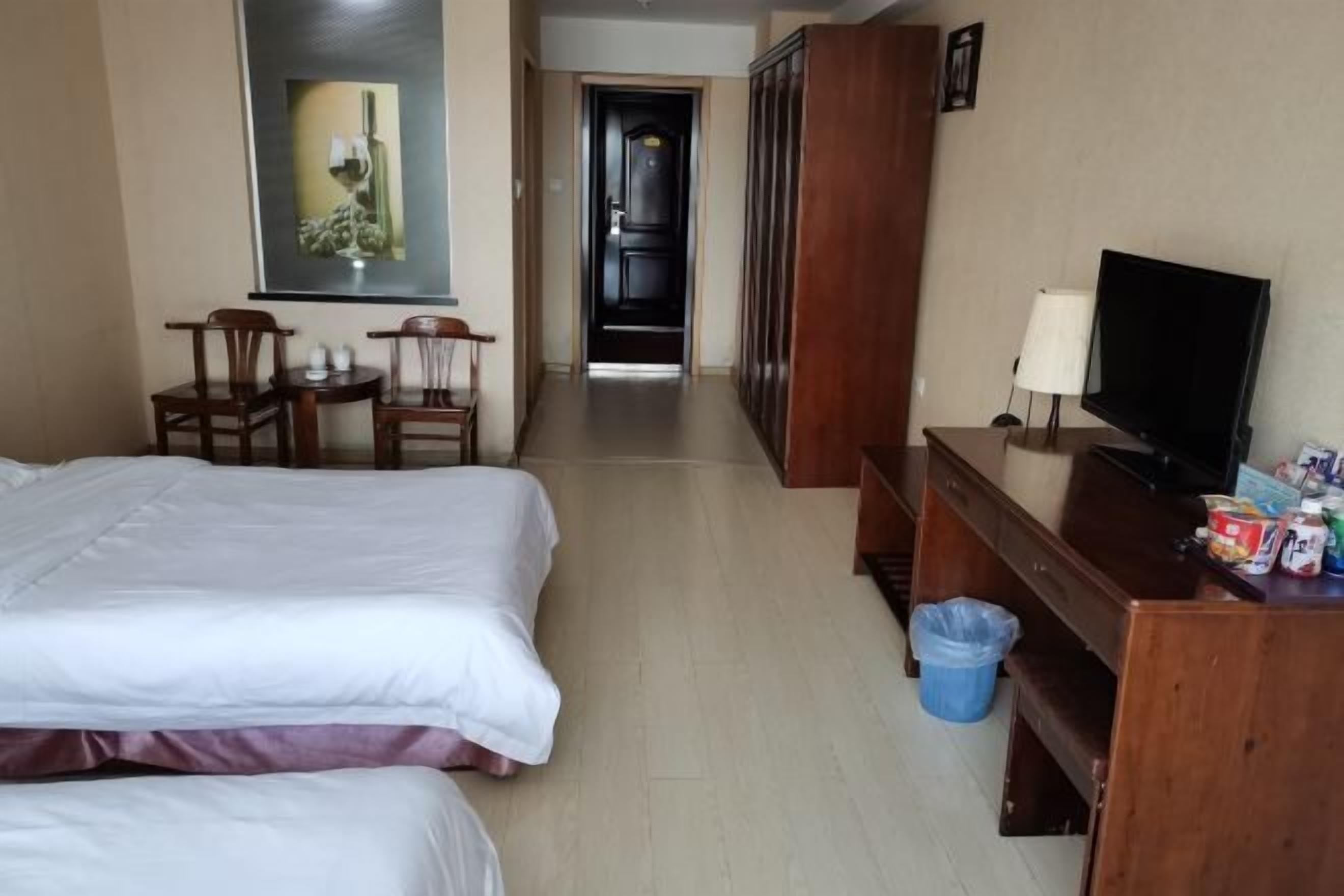 A hotel room with a bed, a desk with a television, a chair, a small table, and a picture on the wall.