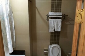 A bathroom with a toilet, a towel rack with towels, and a shower curtain.