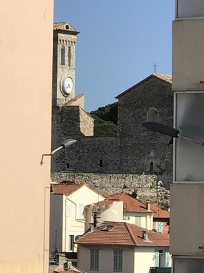 Un edificio storico in pietra con una torre dell'orologio, circondato da edifici residenziali con tetti in tegole rosse.