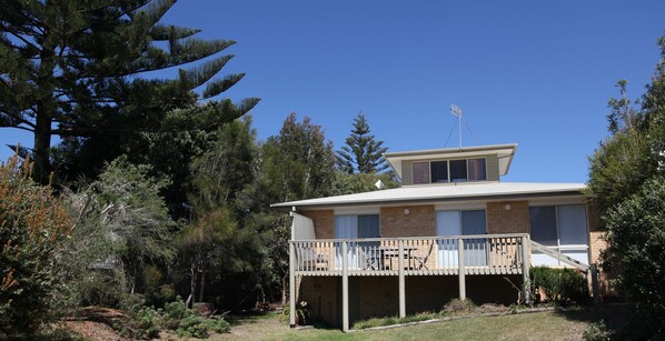 Uma casa de dois andares com varanda, rodeada por árvores e um gramado.