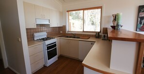 Eine kleine Küche mit weißen Schränken, einem Gasherd, einem Backofen, einer Spüle und einem Fenster mit Jalousien.