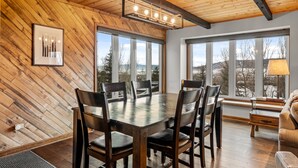 A dining area with a wooden table and chairs, large windows with a view, and a ceiling with exposed beams. - Winterset 3 3 Bedroom Condo by RedAwning (Steamboat Springs)